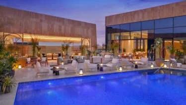 Rooftop terrace at The St. Regis Riyadh featuring a blue swimming pool and white lounge chairs under warm