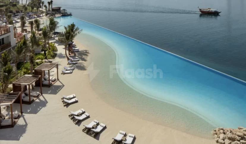 Infinity pool at Dubai Creek Golf & Yacht Club in Dubai, bordering a white sand beach with wooden cabanas