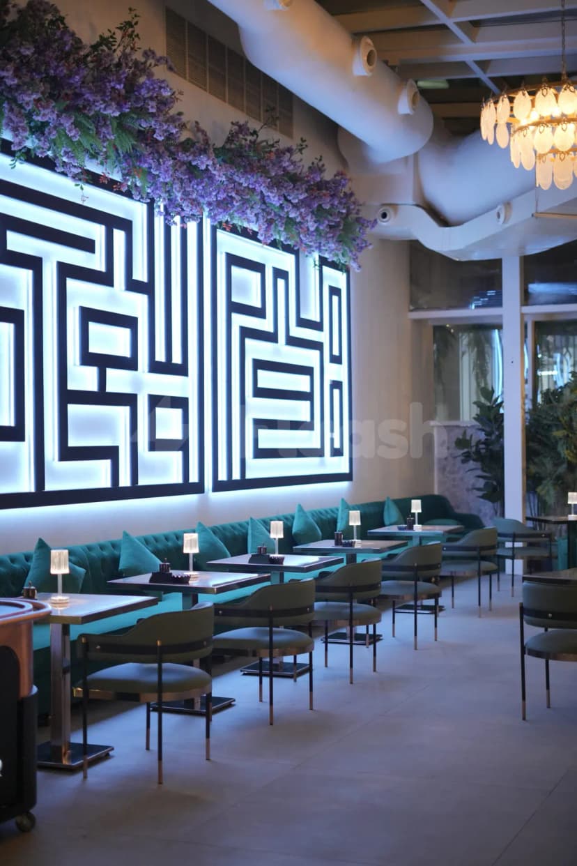 Illuminated geometric wall art and purple floral arrangement at Coco Restaurant Al Murooj in Dubai, featuring green velvet
