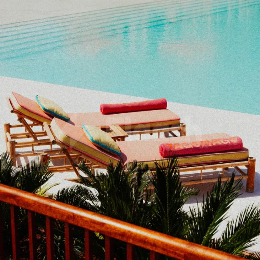 Rooftop terrace at Tagomago Dubai featuring a turquoise swimming pool and wooden lounge chairs with rolled pink towels