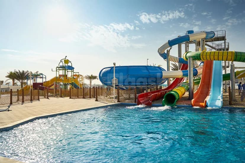 Swimming pool at Hotel Riu Dubai featuring multiple water slides and a shallow splash zone under clear skies