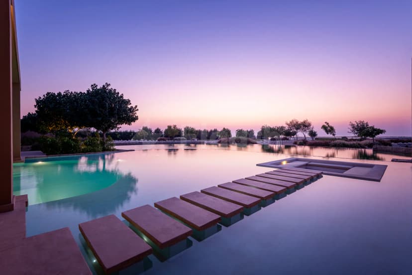 Infinity pool at Zulal Wellness Resort in Doha featuring stone stepping stones and underwater lighting under a twilight