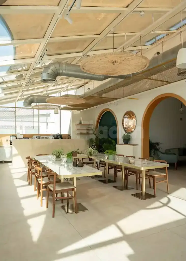 Restaurant interior at Society Restaurant Abu Dhabi featuring marble-top tables, wooden chairs, exposed ductwork, and woven pendant lights