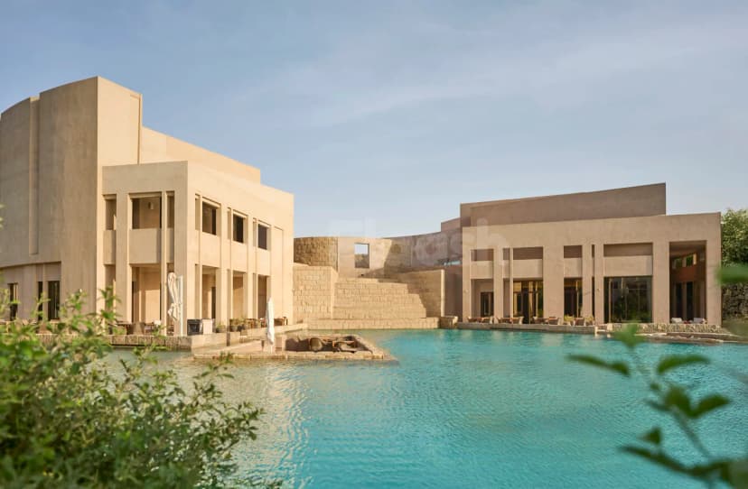 Large swimming pool at Zulal Wellness Resort in Doha, surrounded by beige concrete buildings with stone steps