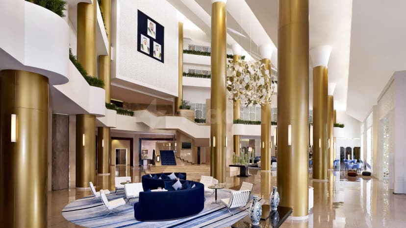 Entrance Hall at Le Meridien Al Khobar featuring gold columns, a large chandelier, and a multi-level staircase