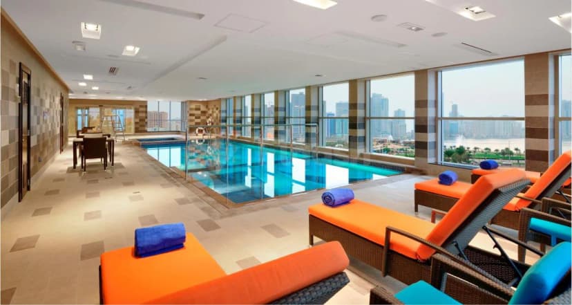 Indoor swimming pool at Al Majaz Premiere Hotel Apartments in Sharjah with glass railing and city skyline view