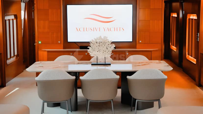 Boardroom on Xclusive 35 Yacht Dubai featuring a marble table, beige upholstered chairs, and a large screen displaying