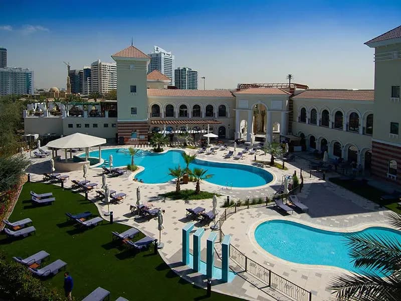 Large curved swimming pool at The Els Club Dubai Sports City with blue decorative pillars