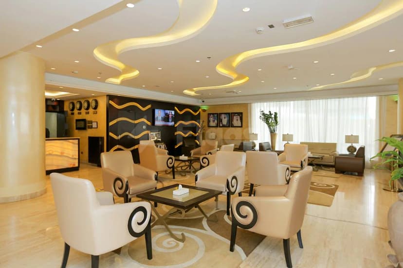 Entrance hall at Ivory Grand Hotel Apartments Dubai featuring cream armchairs with black spiral armrests and a curved