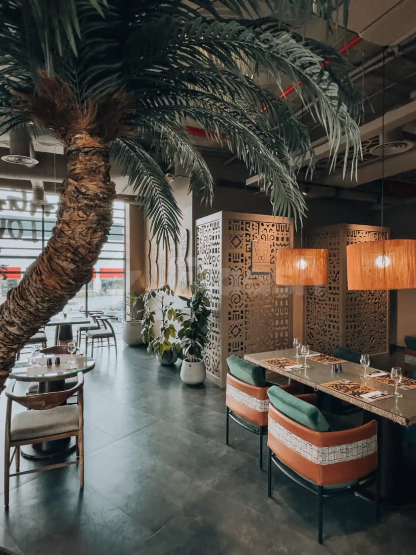 Indoor dining space at Agape Restaurant & Cafe Taif featuring a large palm tree and decorative laser-cut wooden screens