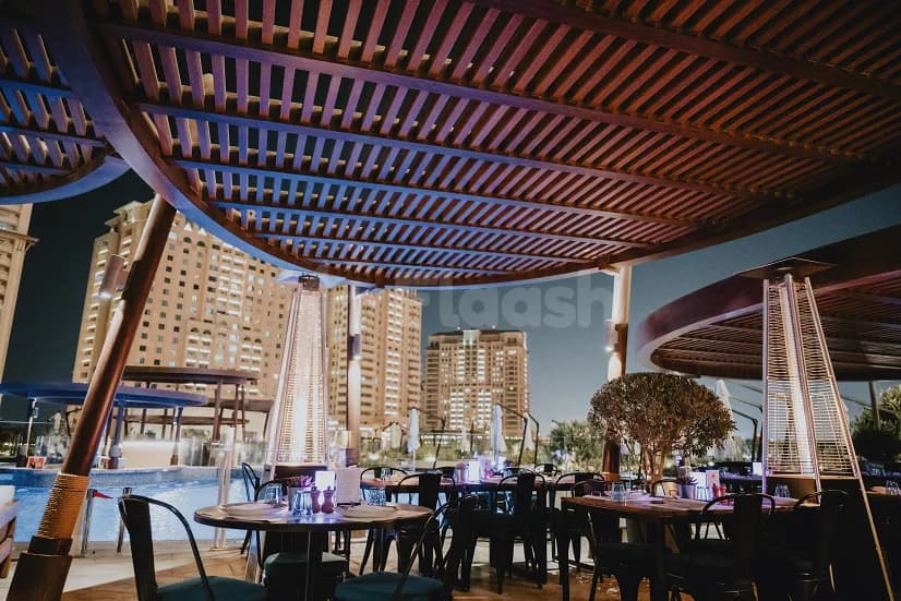 Rooftop terrace at The Kitchen Doha featuring a wooden slatted ceiling and tall patio heaters with city skyline