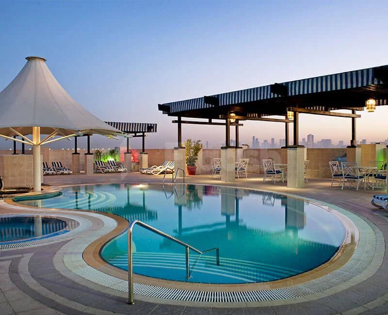 Curved swimming pool at Excelsior Hotel Downtown Dubai with white sunshade canopy and striped awning, city skyline visible