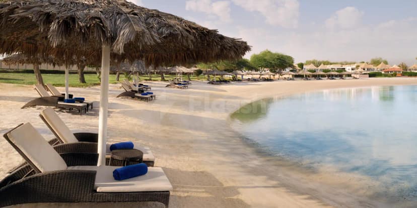 Thatched umbrella and wicker lounge chairs line a sandy terrace beside a shallow pool at InterContinental Al Jubail