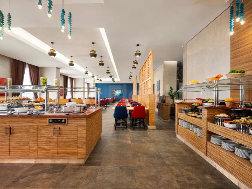 Restaurant at Novotel Thakher in Makkah featuring a long buffet counter with wooden cabinetry and glass sneeze guards