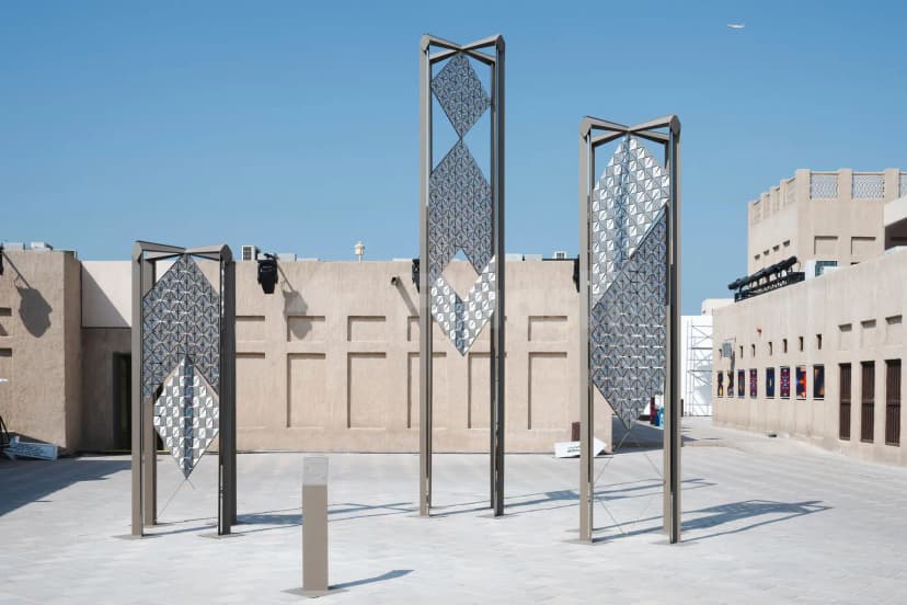 Outdoor courtyard at Alserkal Avenue in Dubai featuring three tall geometric metal sculptures with reflective triangular panels against