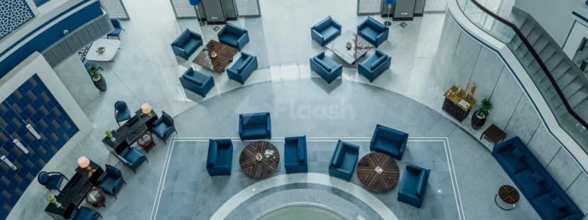 Entrance hall at Retaj Salwa Resort & Spa in Doha featuring circular seating, marble flooring, and a glass-railing staircase