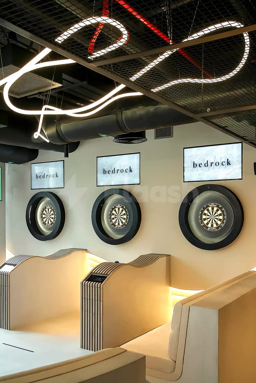 Games lounge at Bedrock Pier 7 in Dubai featuring wall-mounted dartboards and beige curved seating with striped partitions