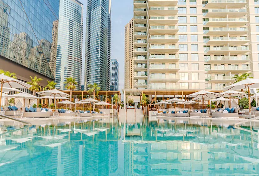 Rectangular swimming pool at Cove Beach Dubai with turquoise water reflecting modern high-rise buildings and white umbrellas