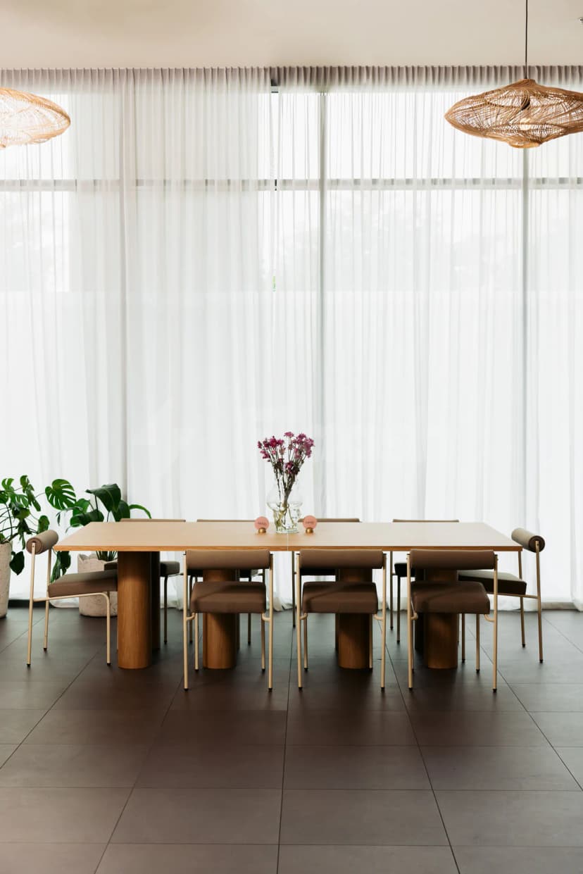 Meeting room at Tania's Teahouse Dubai Hills featuring a long wooden table with cylindrical legs, brown upholstered chairs