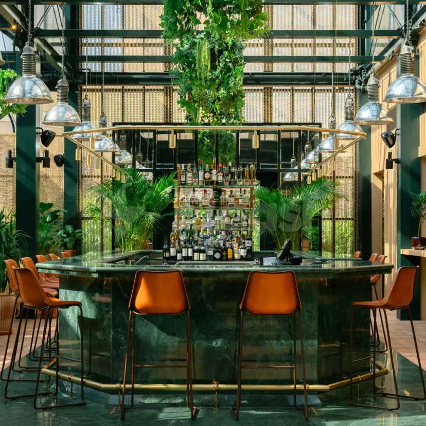 Green marble bar counter at Eugène Eugène Restaurant Dubai with orange leather stools and hanging ivy
