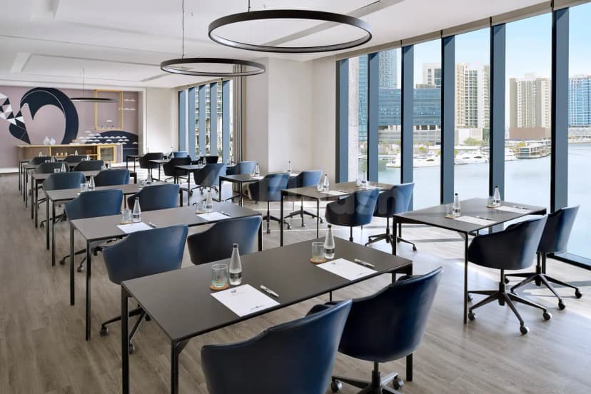 Meeting room at Open Sesame Dubai with black rectangular tables, blue rolling chairs, and large windows overlooking