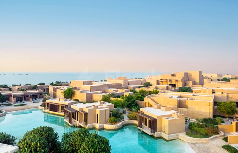 Rooftop terrace at Zulal Wellness Resort in Doha featuring beige stone buildings, a turquoise pool, and coastal views