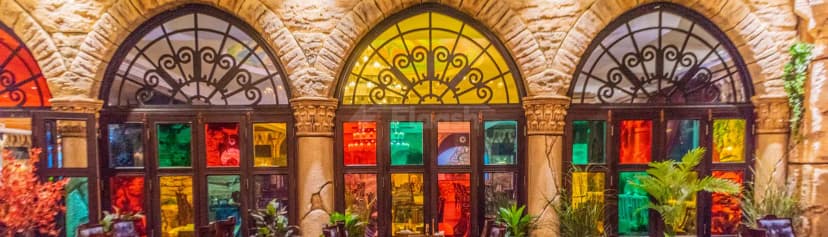 Al Meshwar Restaurant Dubai entrance hall featuring stone walls, arched stained glass windows with ornate black metal grilles
