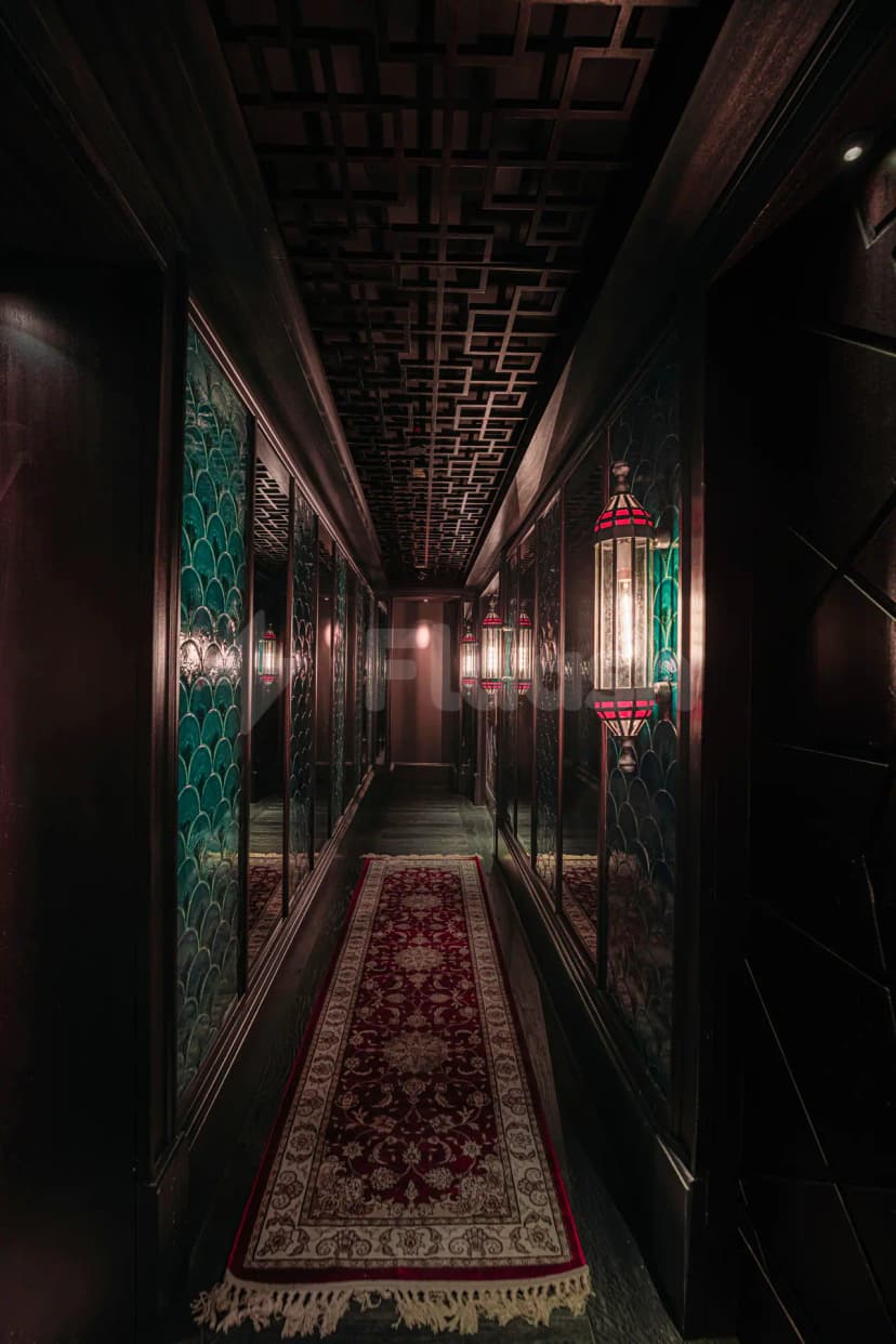 Entrance hall at Hutong Dubai featuring a red patterned rug with fringe and teal fishscale glass panels