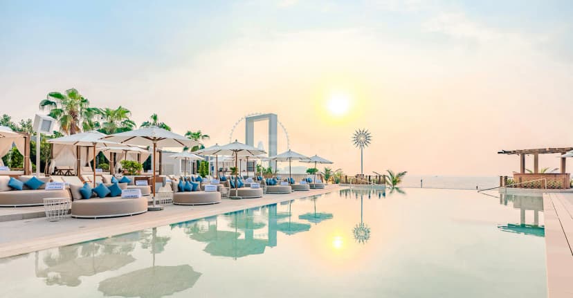 Rooftop terrace at Cove Beach Dubai featuring an infinity pool, white sun umbrellas, and a distant Ferris wheel