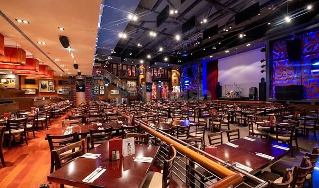 Restaurant interior at Hard Rock Cafe Dubai featuring dining tables, wooden chairs, and a stage area with blue