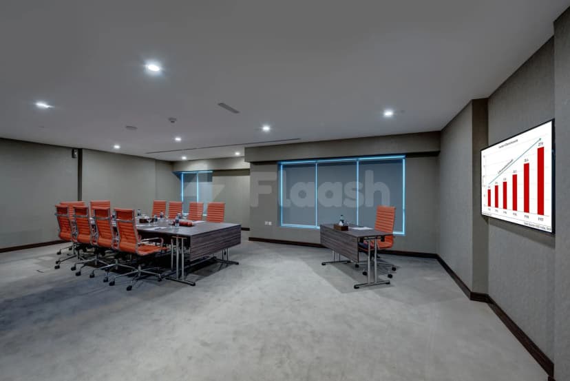Boardroom at Vintage Grand Hotel Dubai featuring a long table, orange chairs, grey carpet, and a wall-mounted display