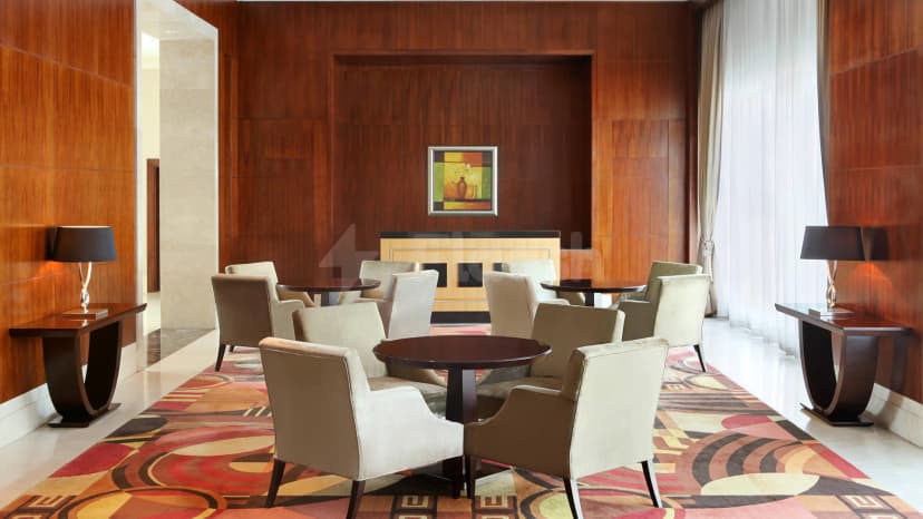 Meeting room at Le Meridien Towers Makkah featuring wooden wall panels, beige armchairs, dark round tables