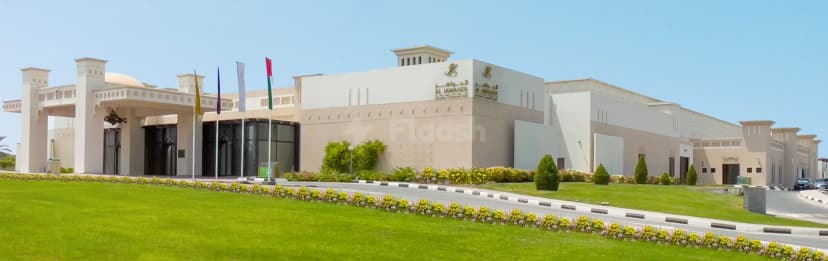 Hotel facade of Al Jawaher Reception and Convention Centre in Sharjah featuring arched entrance, flagpoles, and landscaped green