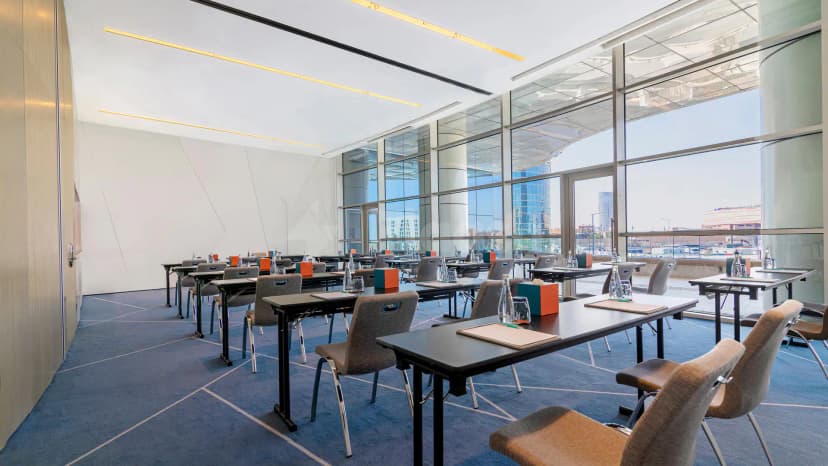 Meeting room at Le Meridien Riyadh with rectangular tables, grey chairs, and large glass windows overlooking the city