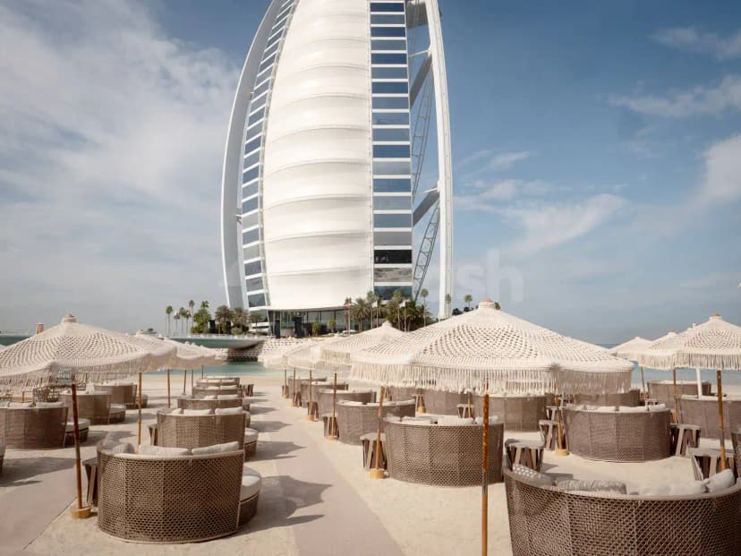 Verde Beach Restaurant Dubai terrace with woven wicker chairs, white fringed umbrellas, and the Burj Al Arab