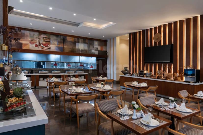 Restaurant at Warwick Hotel Jeddah featuring wooden tables with checkered chairs, an open kitchen, and vertical wood paneling