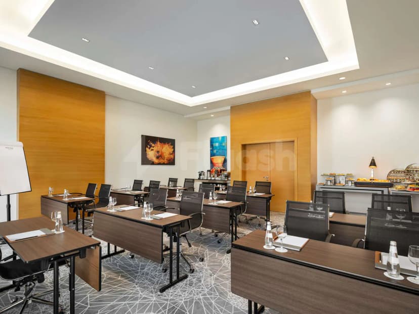 Meeting room at Novotel Thakher Makkah with rectangular tables, black mesh chairs, wooden panels, and a buffet counter
