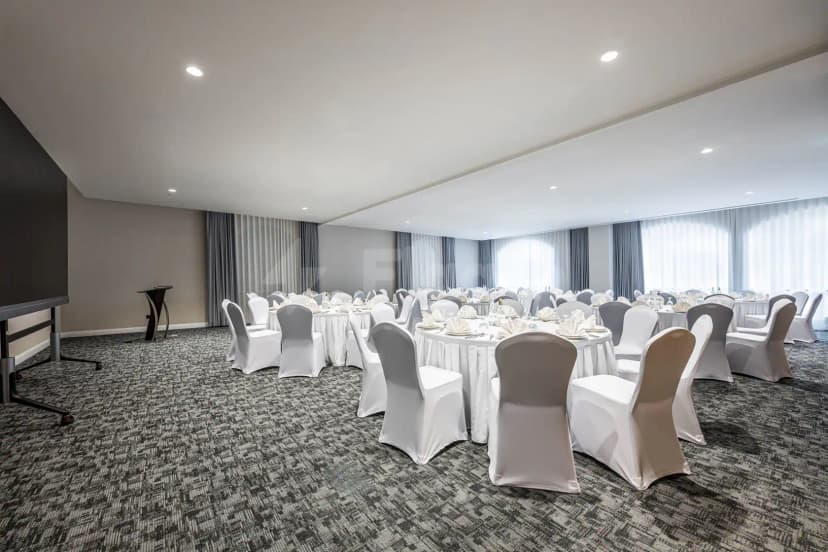 Ballroom at Intercity Hotel Riyadh set with round tables, white chair covers, and grey carpet under recessed ceiling
