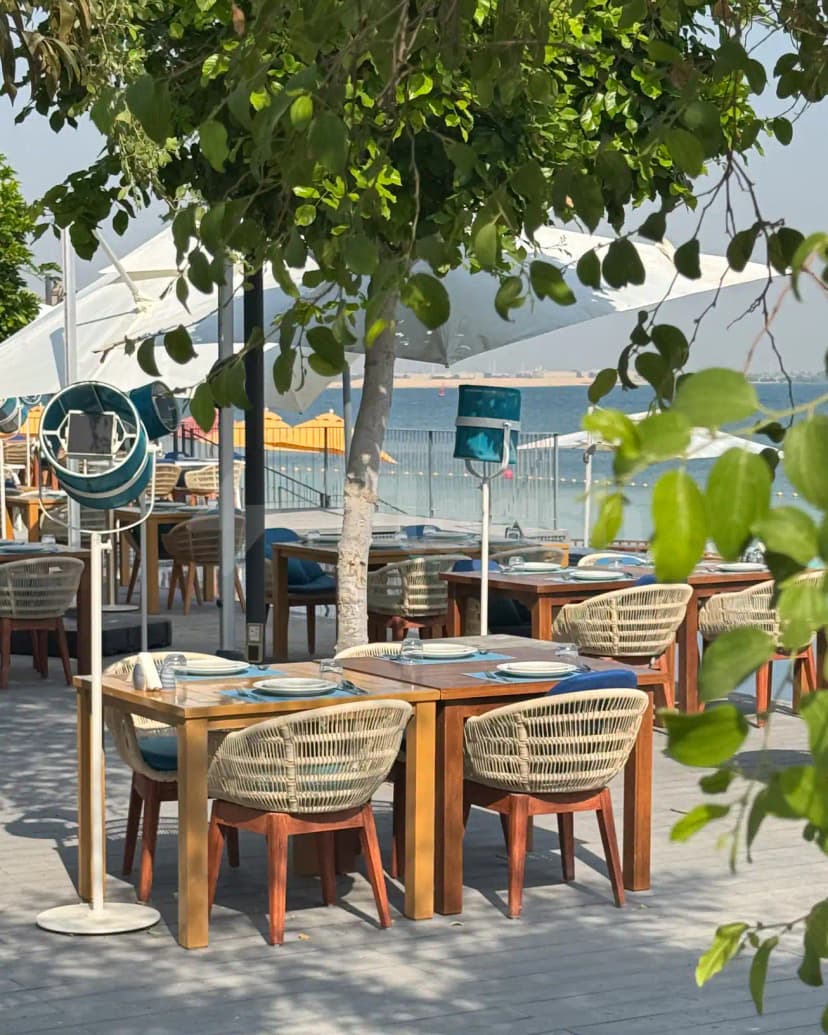Terrace at Ibn AlBahr Seafood Restaurant in Dubai with wooden tables, wicker chairs, and a sea view under