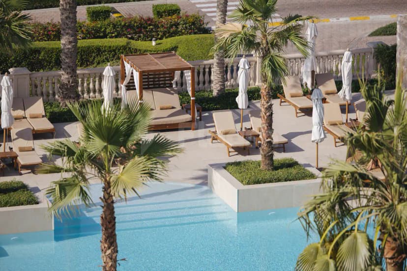 Rectangular swimming pool at Jumeirah Golf Estates in Dubai, surrounded by palm trees and a wooden cabana
