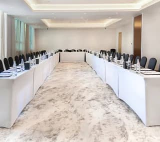 Meeting room at Swissotel Al Murooj Dubai with long rectangular tables, black chairs, marble floor, and recessed ceiling