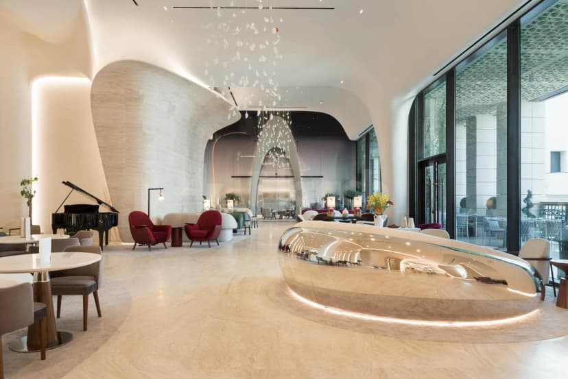 Entrance hall at Sanad Lounge Doha featuring a curved stone wall and a reflective metallic reception desk