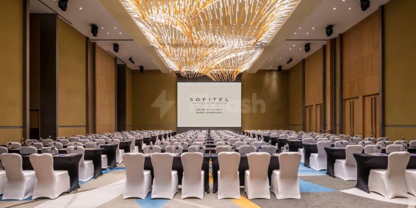 Ballroom at Sofitel Dubai Downtown with rows of tables, white chair covers, and a large illuminated chandelier