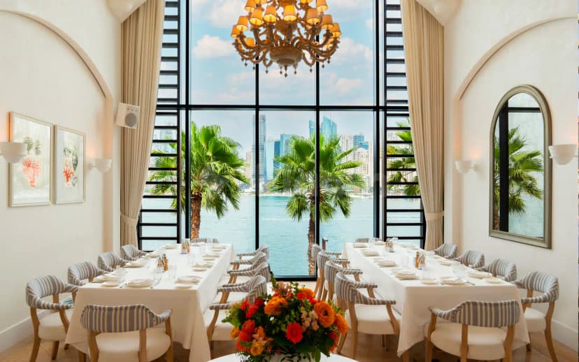 Alici Restaurant Dubai dining room with long tables set for service, large floor-to-ceiling windows framing a waterfront
