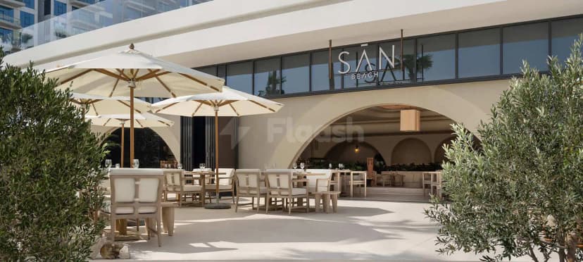 Terrace at San Beach Dubai featuring outdoor dining under cream umbrellas with wooden poles and an arched entrance