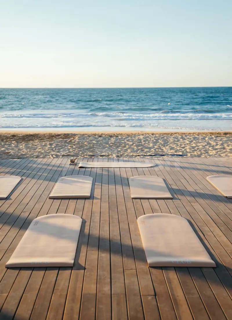Wooden deck at La Cantine Beach in Dubai set with beige yoga mats overlooking the ocean and sandy