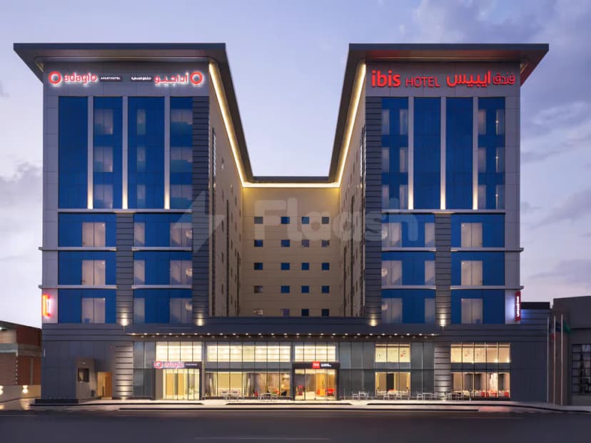 Hotel facade of Adagio Jumeirah Village Triangle in Dubai featuring illuminated ibis and adagio signage with blue glass