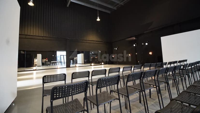 Meeting room at Sima Performing Arts Dubai with black perforated chairs, a white projection screen, and mirrored wall