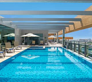 Rooftop terrace at Swissotel Living Jeddah featuring a rectangular swimming pool with blue mosaic tiles and a glass