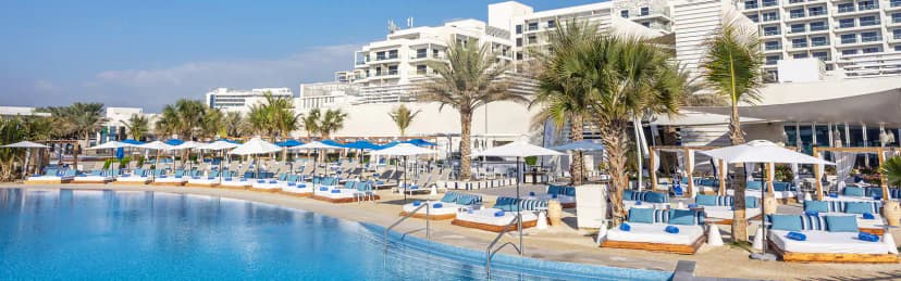 Large swimming pool at Cafe del Mar Beach Club Abu Dhabi with palm trees and modern white building